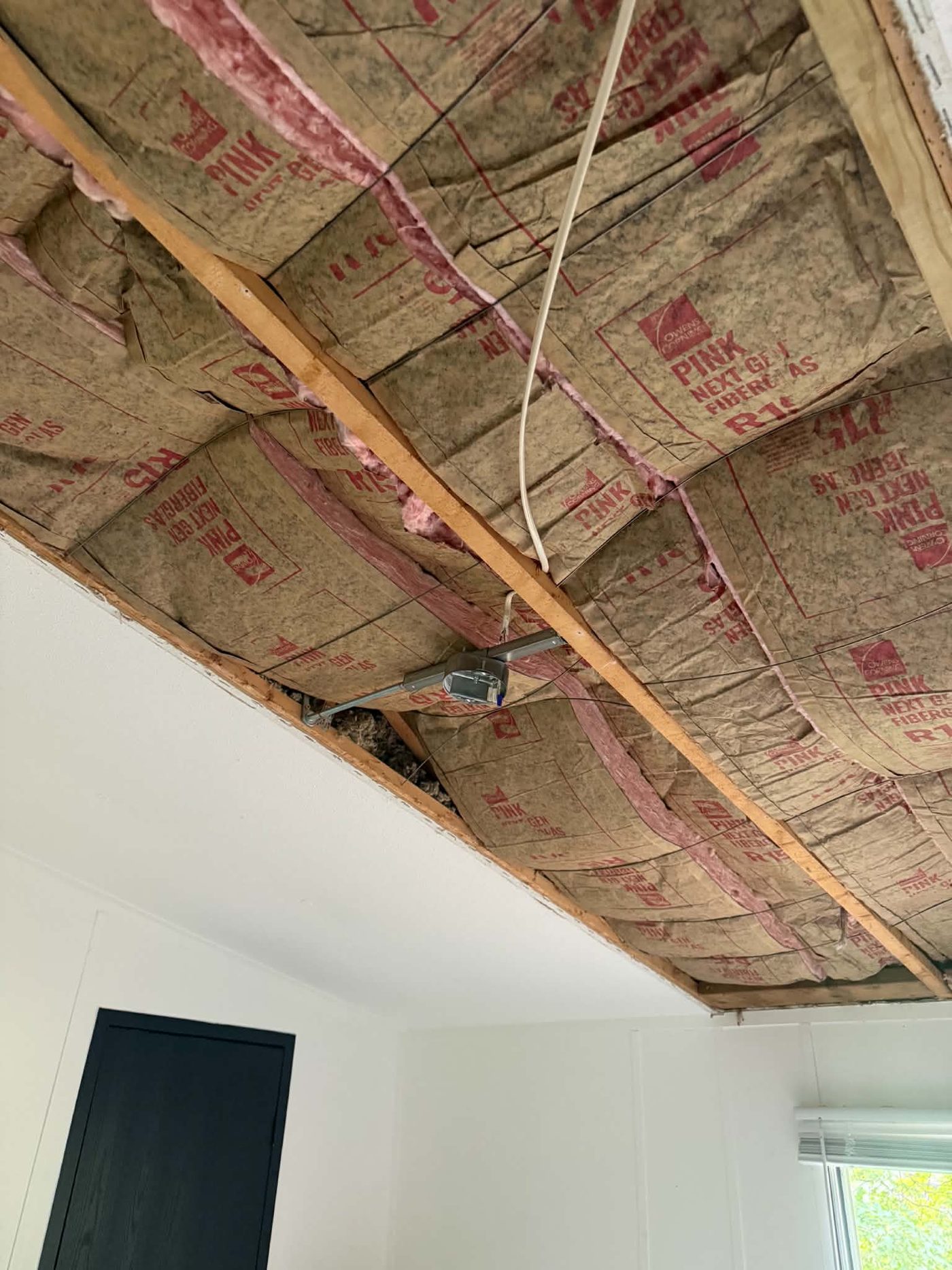 Ceiling opened along a run, exposing joists, kraft-faced fiberglass insulation and a metal junction box