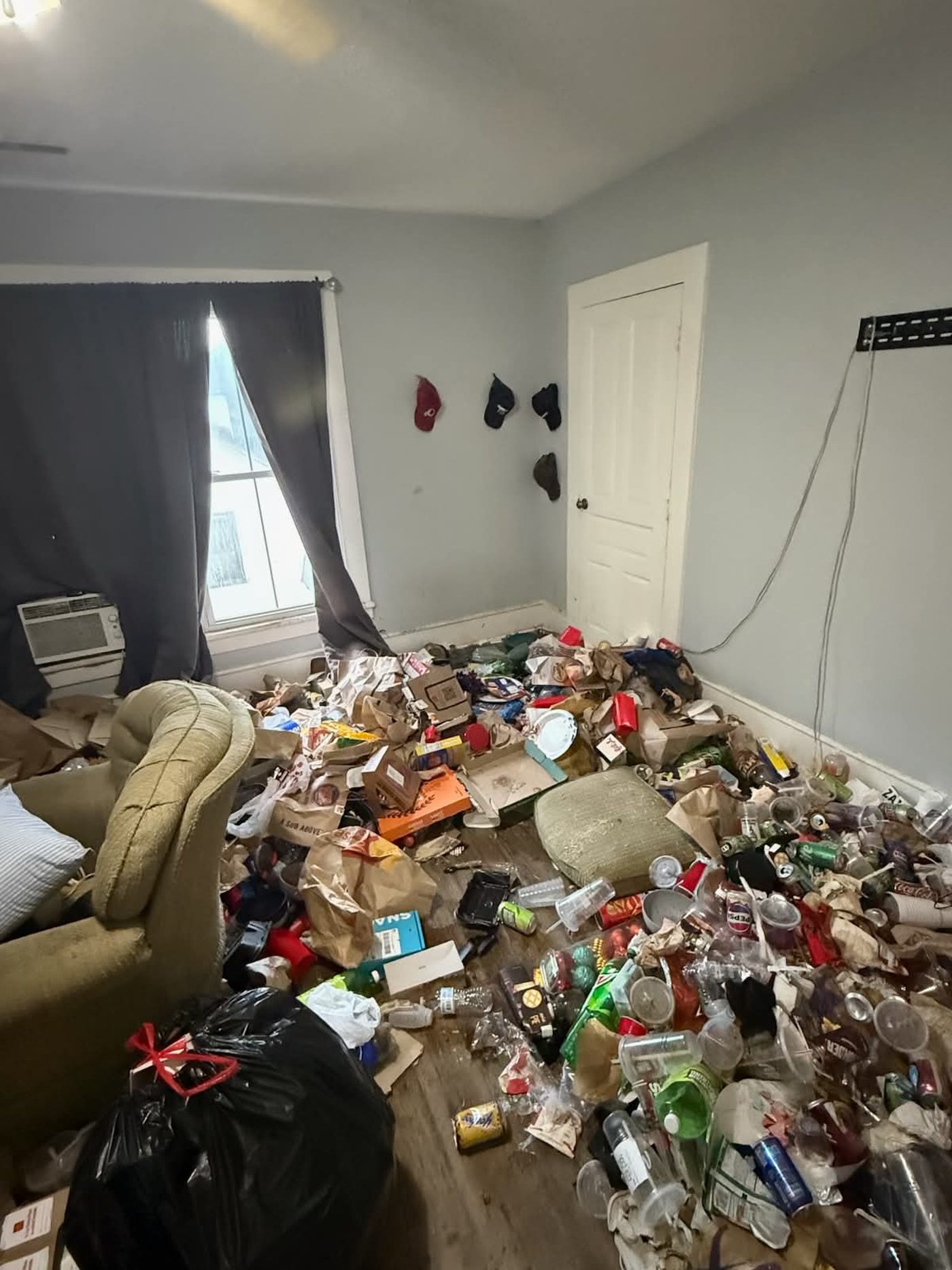 Bedroom floor completely covered in cans, food packaging and household debris, with a recliner half buried